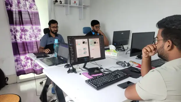 three men working at desks in an office with multiple computer monitors