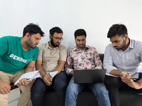 four men sitting together reviewing work on a laptop and taking notes
