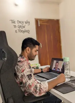 man working at a desk on a laptop during a video call with a wall quote behind him he look like ceo