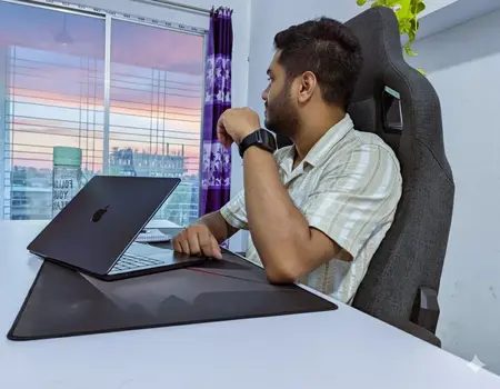 man sitting at a desk with a laptop looking out a window at sunset